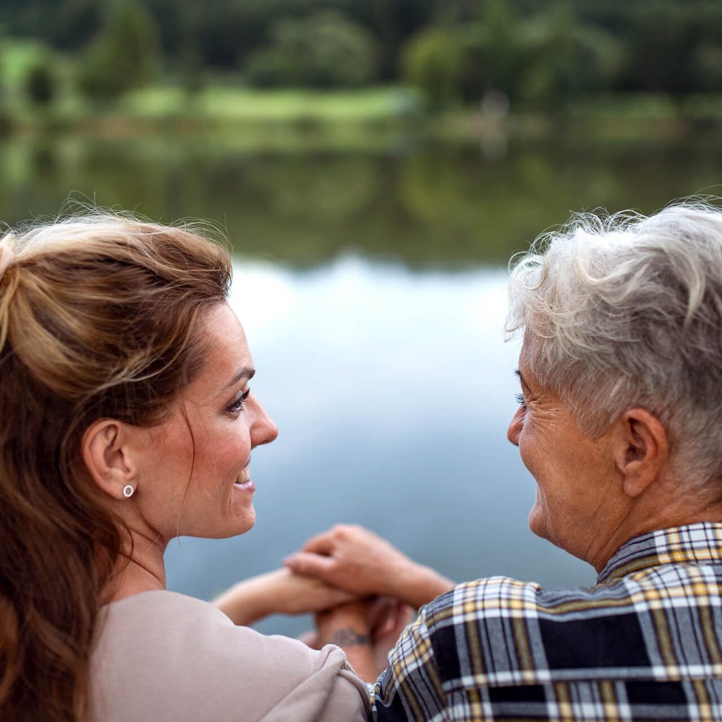 Eine Dame und Seniorin schauen sich an und sitzen am Wasser